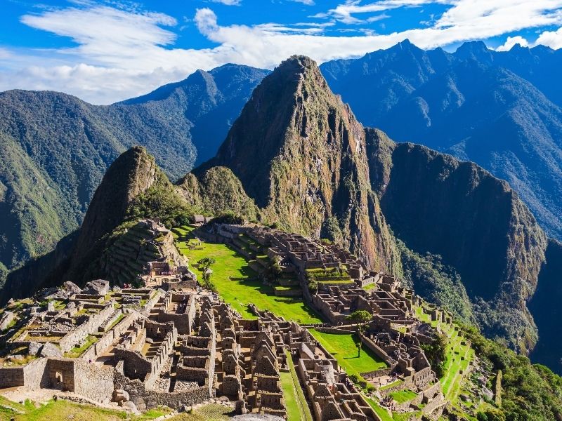 green plateau with brown ancient buildings and blue and green mountains