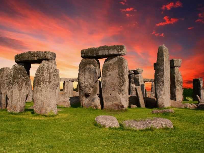 ancient standing rocks infront of a pink and orange and blue sky